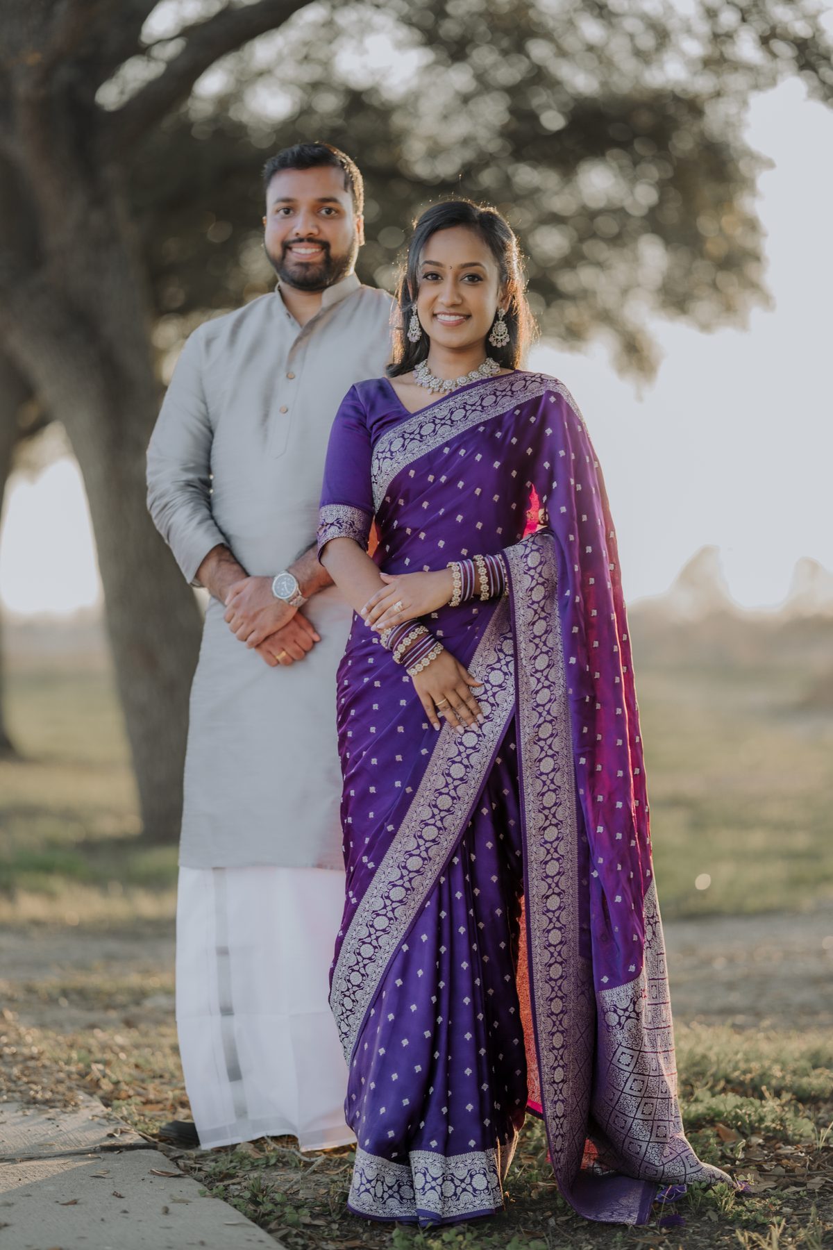 A couple standing under a large tree, in cream and purple